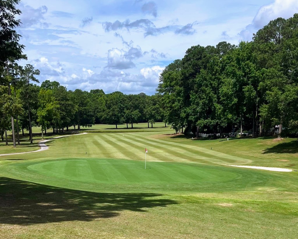 Manicured golf course green with cart path and trees